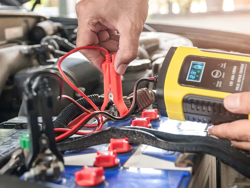 Technician connecting a digital battery tester to a car battery