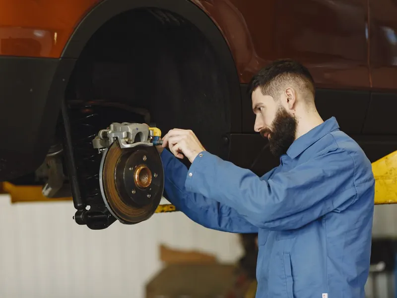 Technician in blue overalls fitting a brake caliper to a disc on a raised car