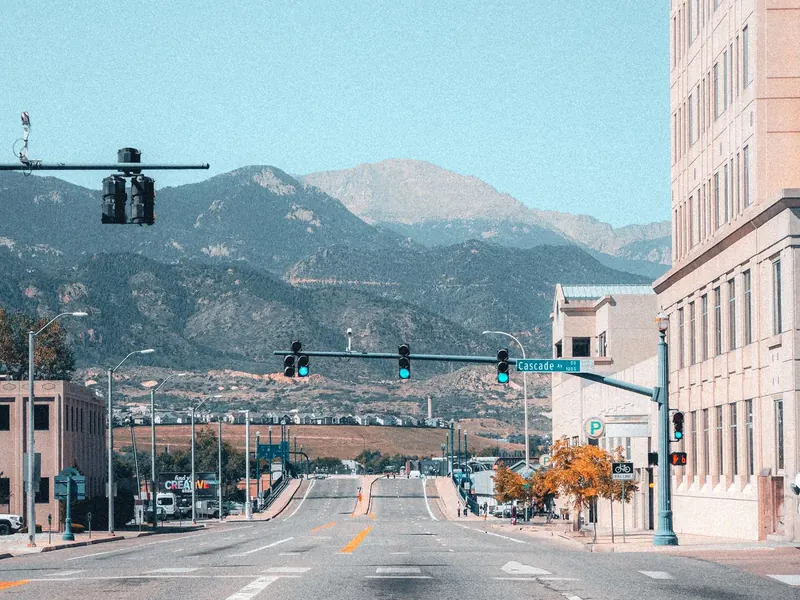 City street with traffic lights and buildings leading toward snow-capped mountains
