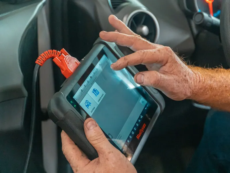 Technician's hands holding a diagnostic tablet connected to a car's dashboard port