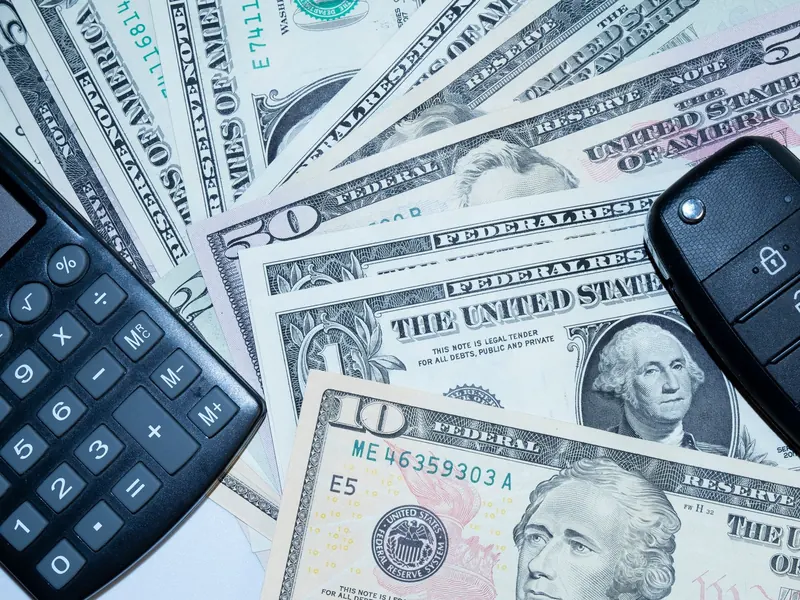 Calculator and car key fob resting on a spread of dollar bills
