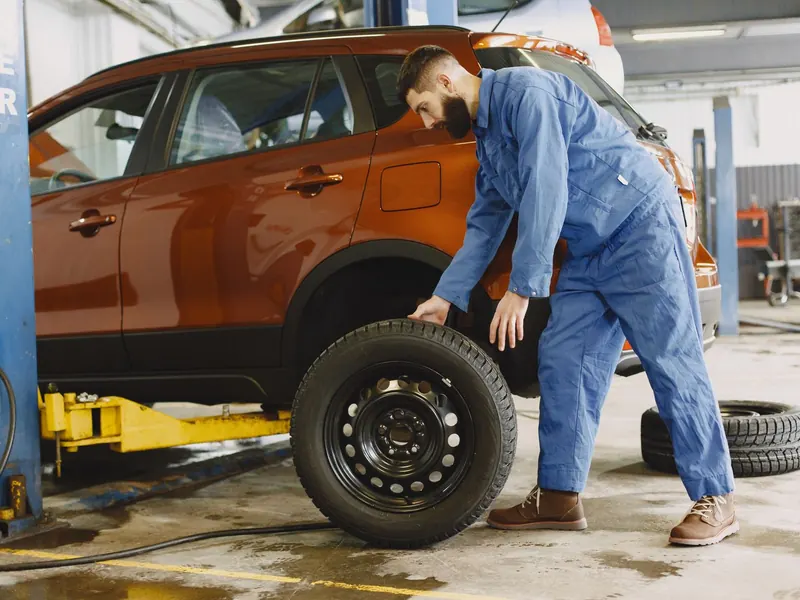 Technician in blue overalls checking the tyre of an orange SUV on a lift