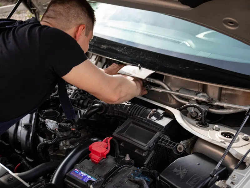 Technician leaning under an open bonnet working on an engine