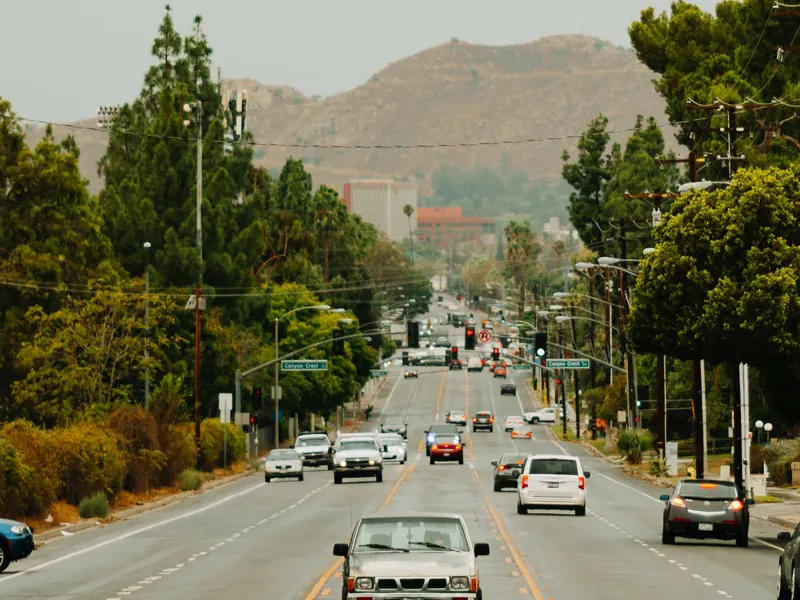Tree-lined road leading toward hills with cars driving in both directions