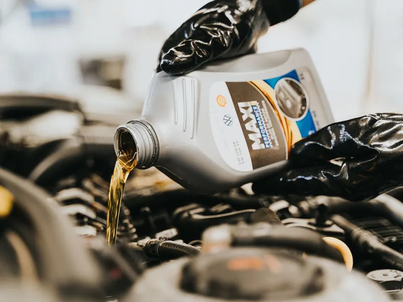 Gloved hands pouring fresh engine oil into an engine filler opening