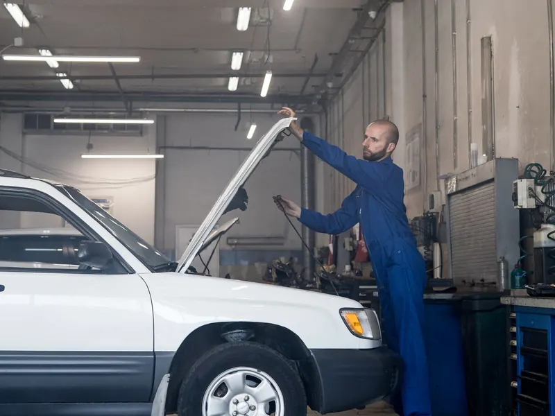 Technician working beside a white car raised on a lift in a modern workshop