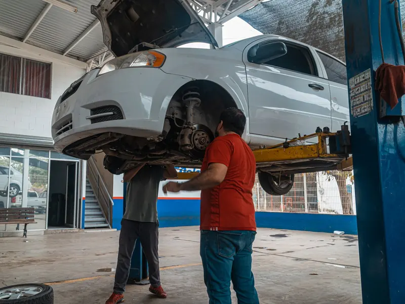 Two technicians inspecting the underside of a white car on a lift
