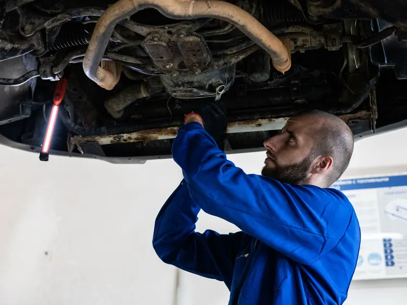 Technician working under a raised car with a work light in a bright workshop