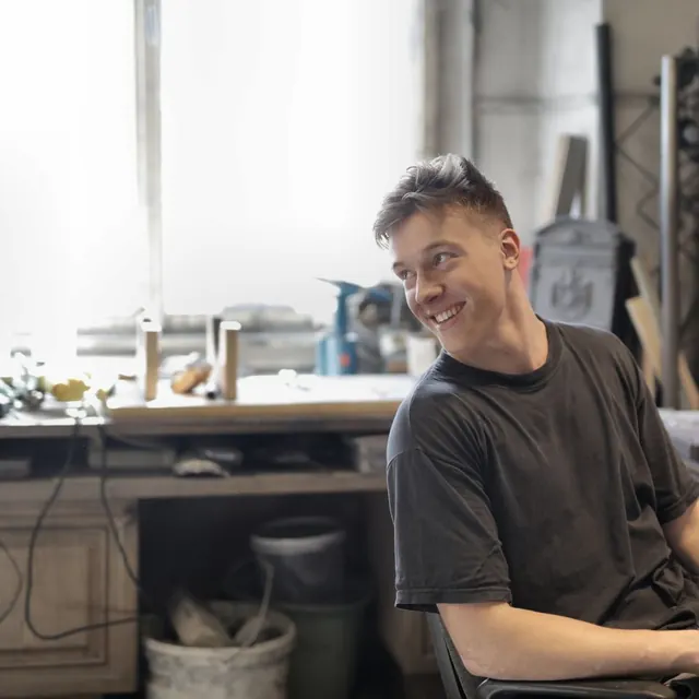 Smiling man in a grey T-shirt sitting at a workbench in a workshop