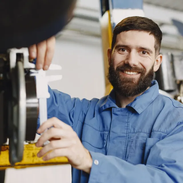 Smiling bearded technician in blue overalls in a workshop
