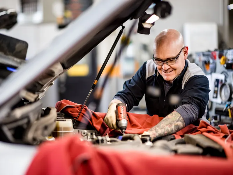 Smiling technician in safety glasses working in an engine bay under a raised bonnet