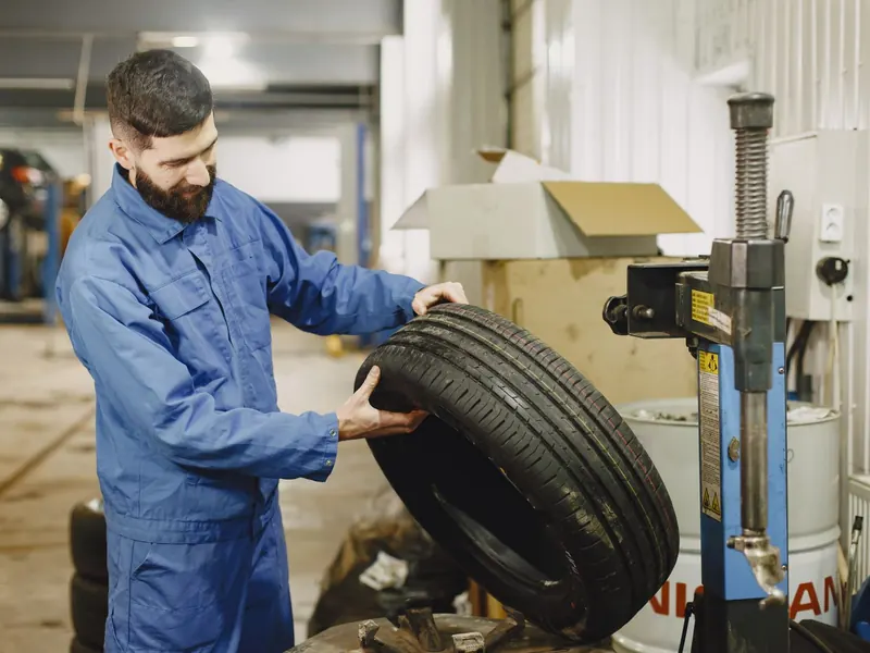 Technician holding a new tyre beside a tyre-fitting machine