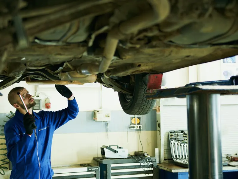 Technician inspecting the underside of a car on a lift with a torch
