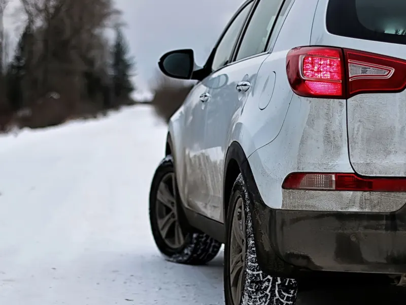 White SUV parked on a snow-covered country road lined with trees