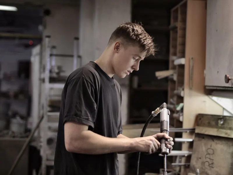 Young technician in a black T-shirt using an air tool in a workshop